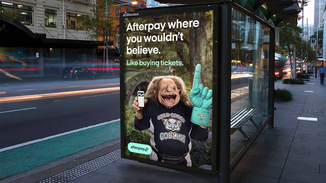 A bus stop billboard, featuring a troll smiling at the camera holding a phone with a funny message: "Afterpay where you wouldn't believe. Like the dentist".