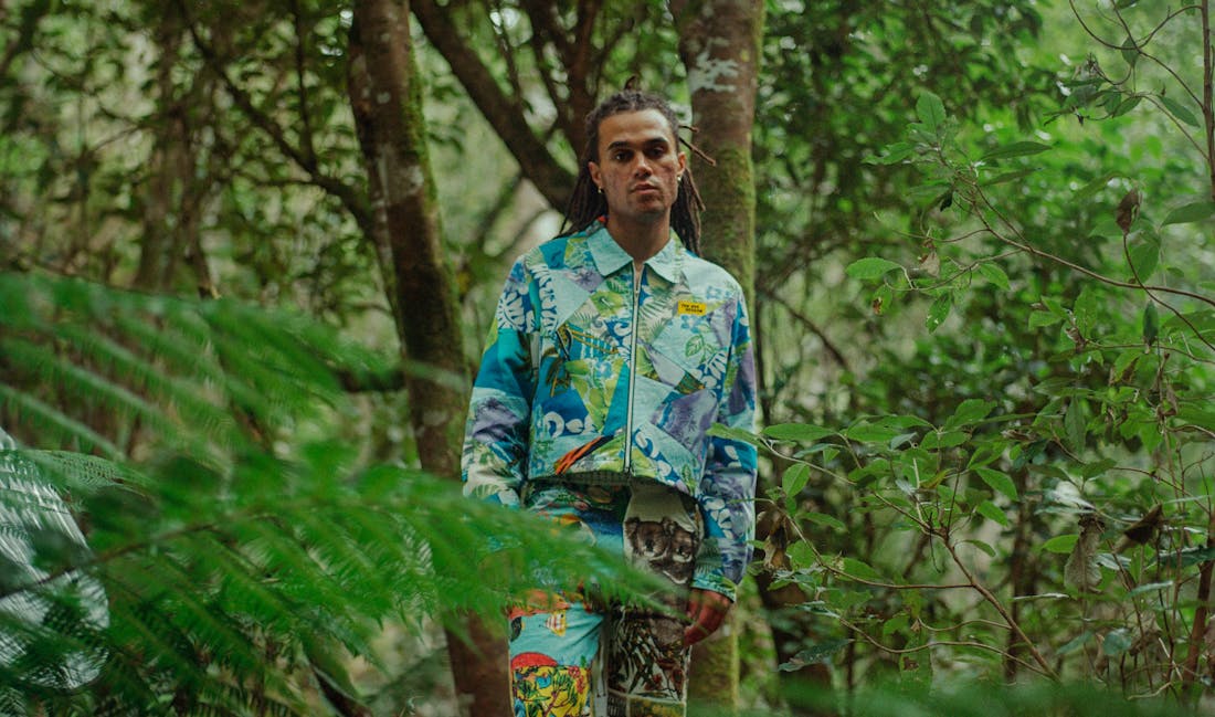 An image of a man standing in a rainforest wearing a vibrant jacket.