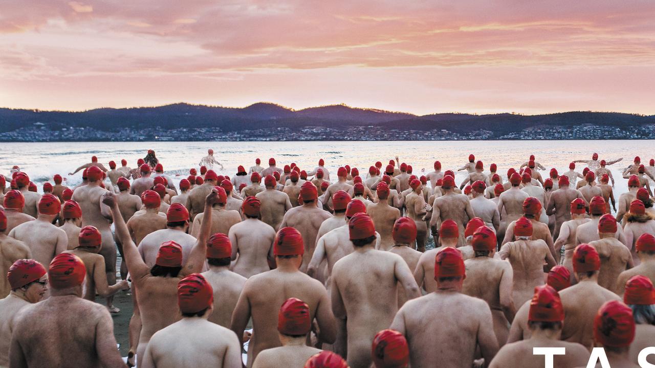 An image of a large group of people in red swimming caps, wading into a serene lake at sunrise to go skinny dipping.