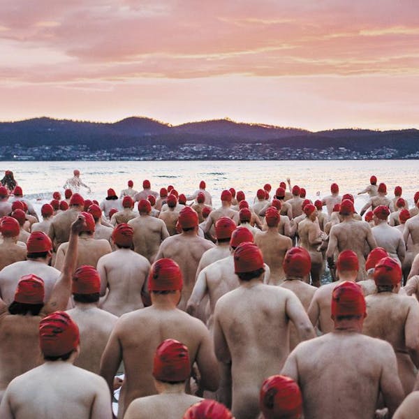 An image of a large group of people in red swimming caps, wading into a serene lake at sunrise to go skinny dipping.