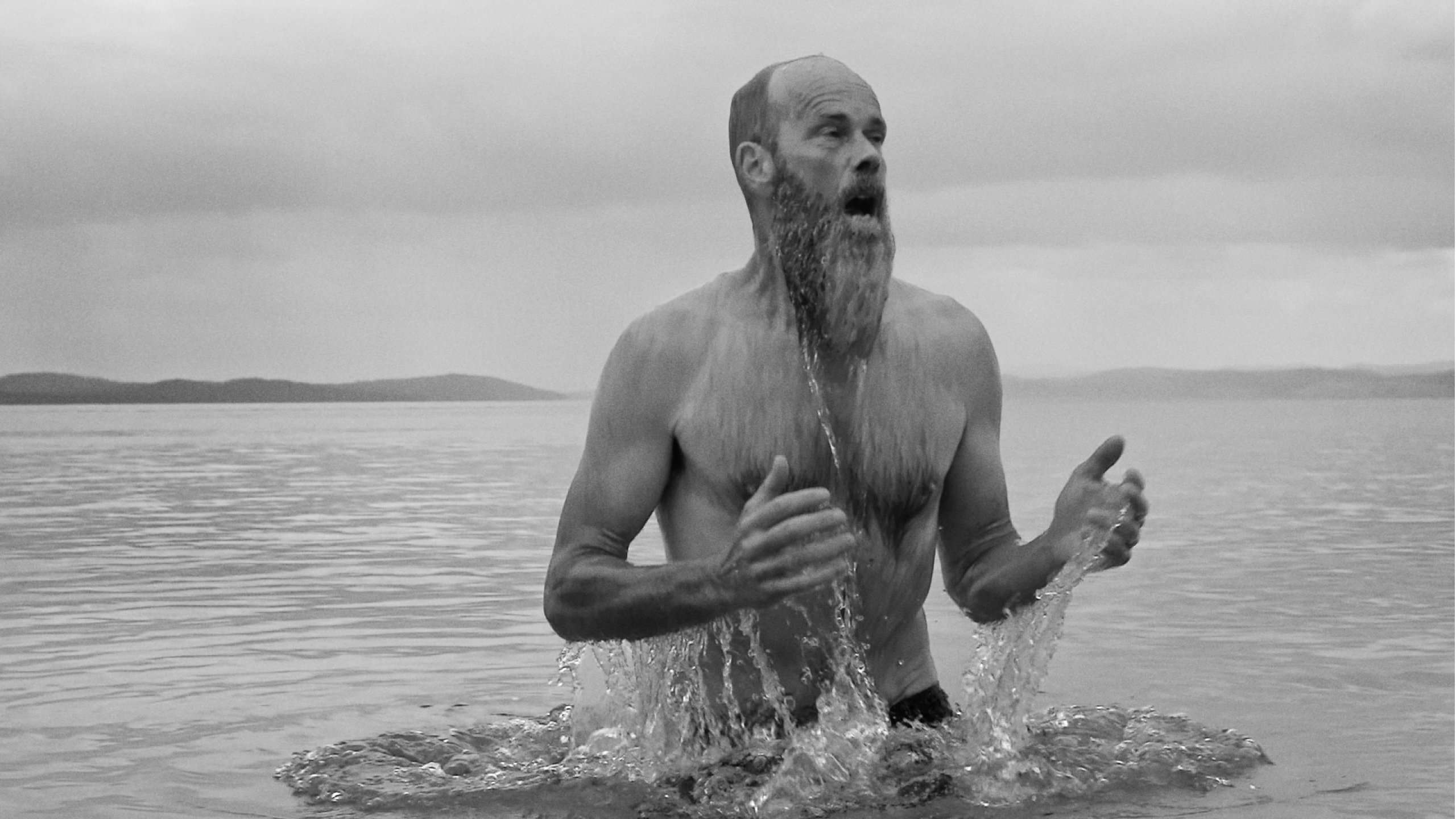 A black and white image of a man with a beard emerging from water.