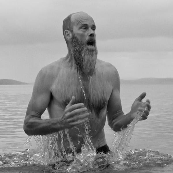 A black and white image of a man with a beard emerging from water.