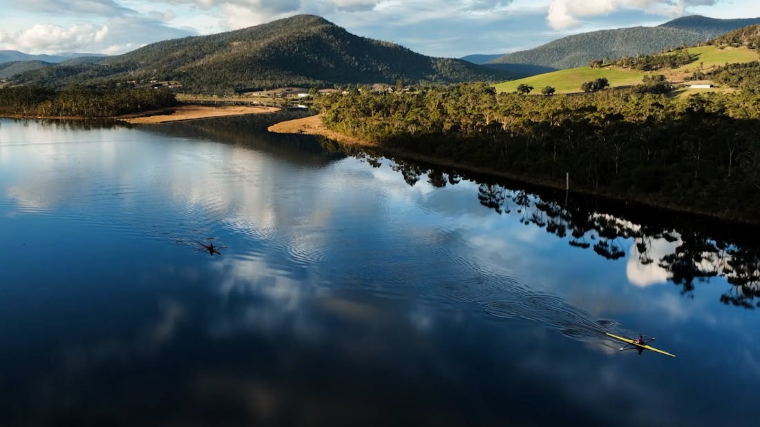 An image of two people rowing on a serene river.