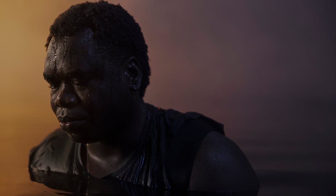 A close-up portrait of a man standing chest deep in water with his head lowered.