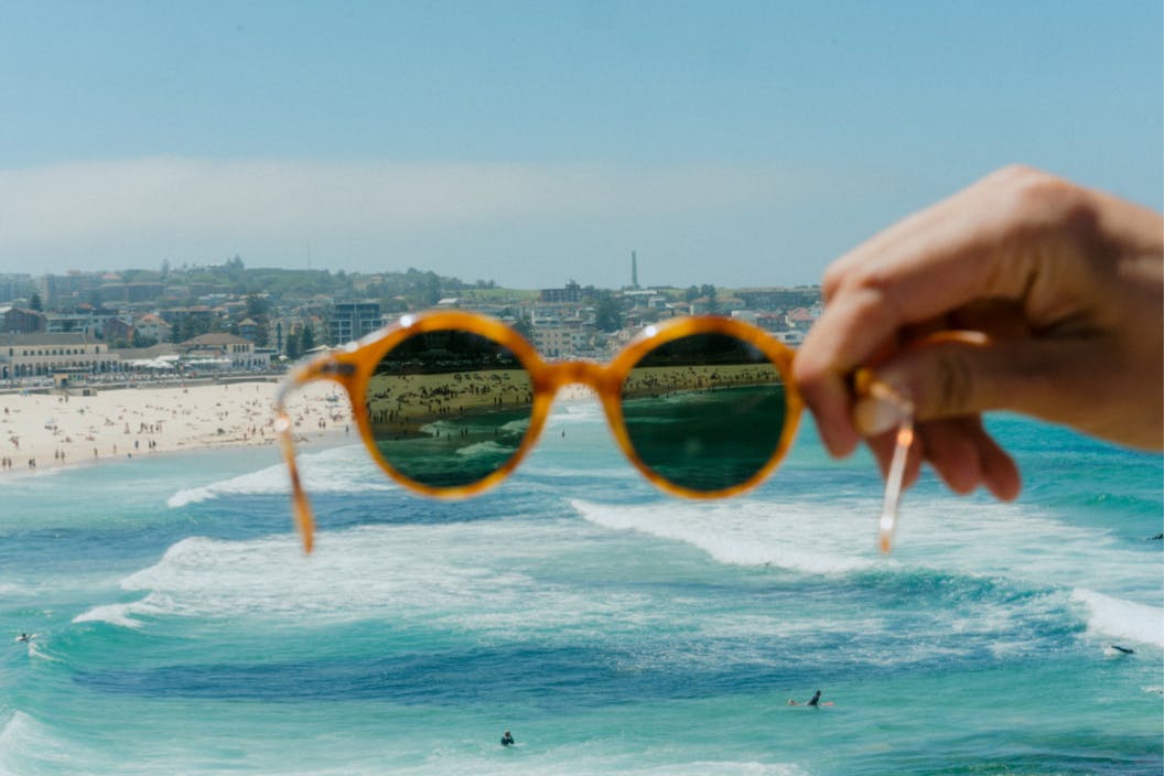 Hand holding up sunglasses in front of Bondi Beach ocean view