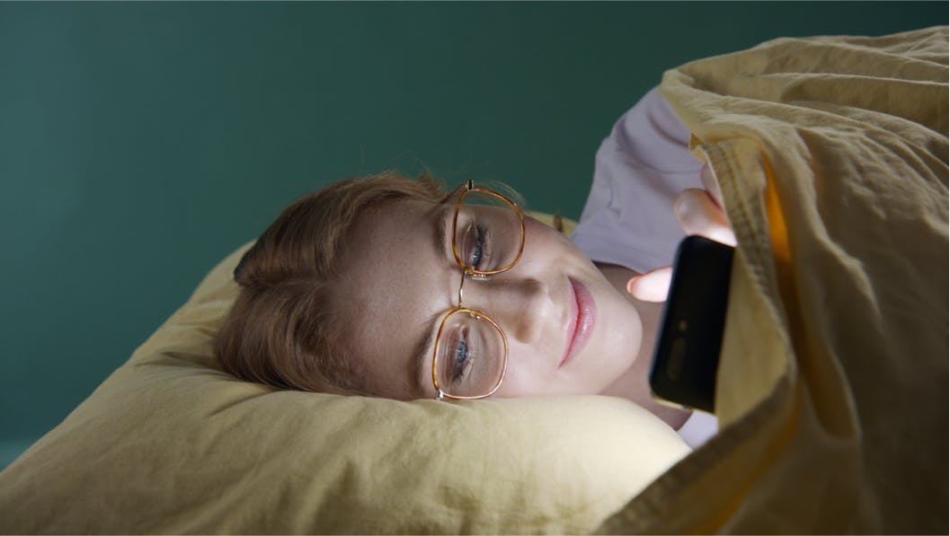person lying in bed staring at phone with light reflecting on face
