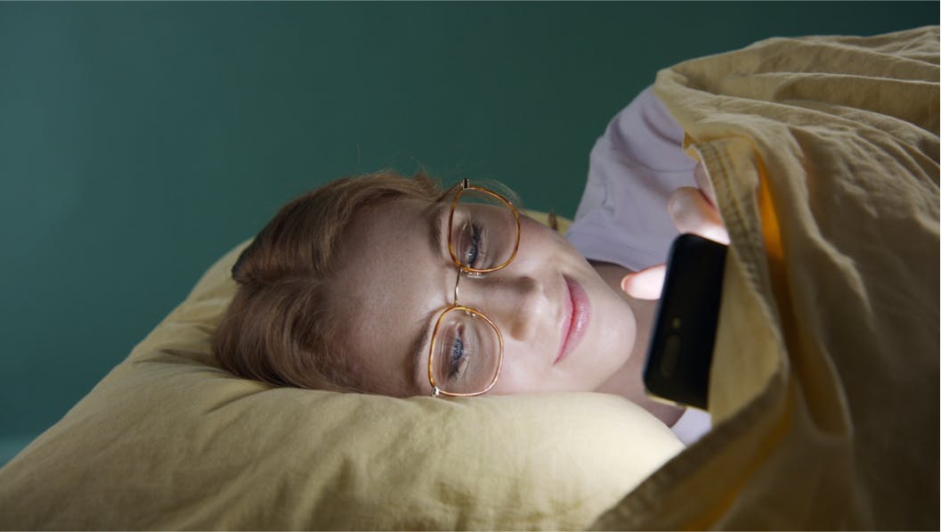 Person lying in bed staring at phone with light reflecting on face