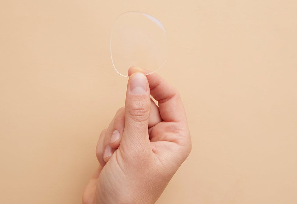 A hand holds up a blank optical lens sample