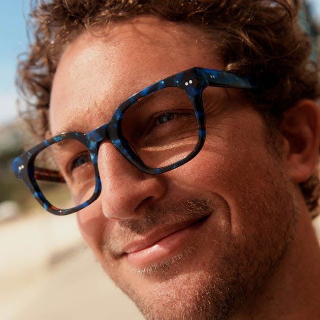 A person wearing square blue acetate Bailey Nelson Dustin glasses in Blue Abalone