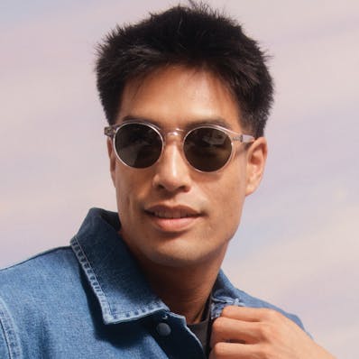 A man wearing round acetate frame clear Bailey Nelson sunglasses with grey lenses.