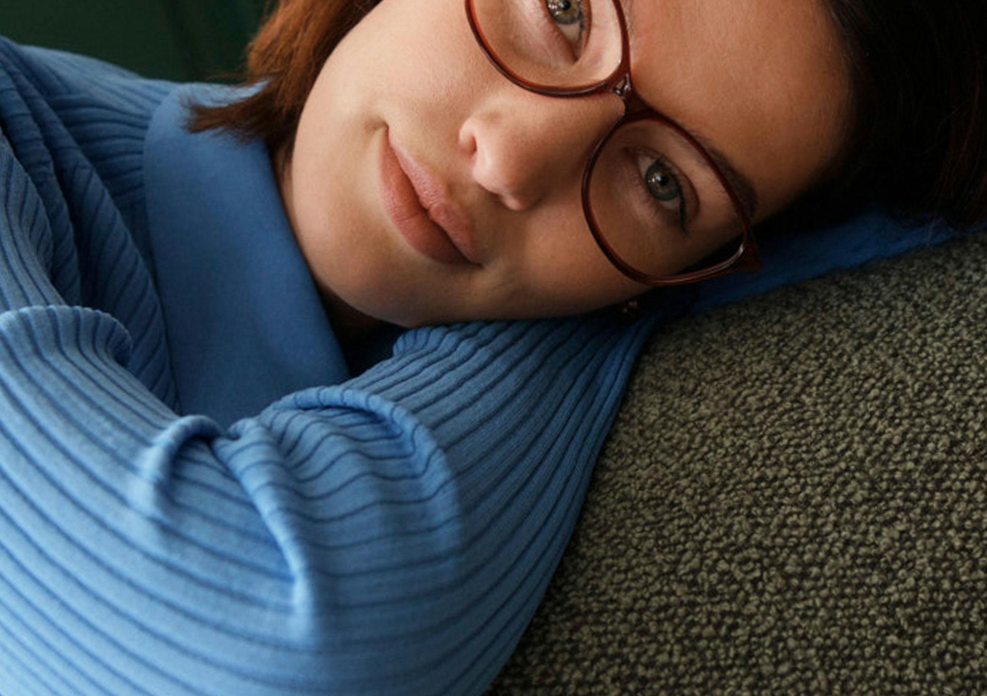 A person wearing red cat eye Bailey Nelson Carrie II Small glasses in Bordeaux, laying their head on their hands.