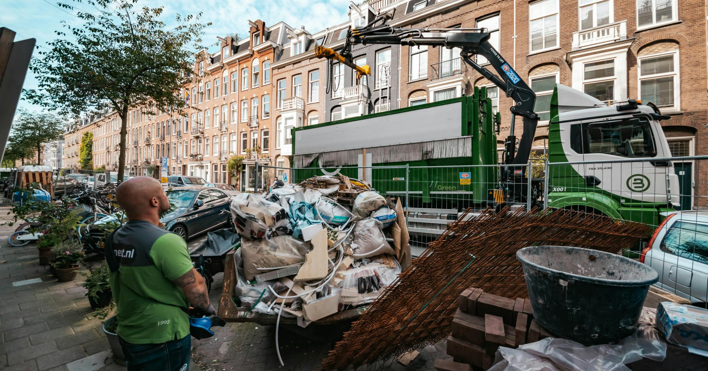 Bnext.nl ophaalwagen in een drukke stadstraat om een container te legen vol met bouw en sloopafval