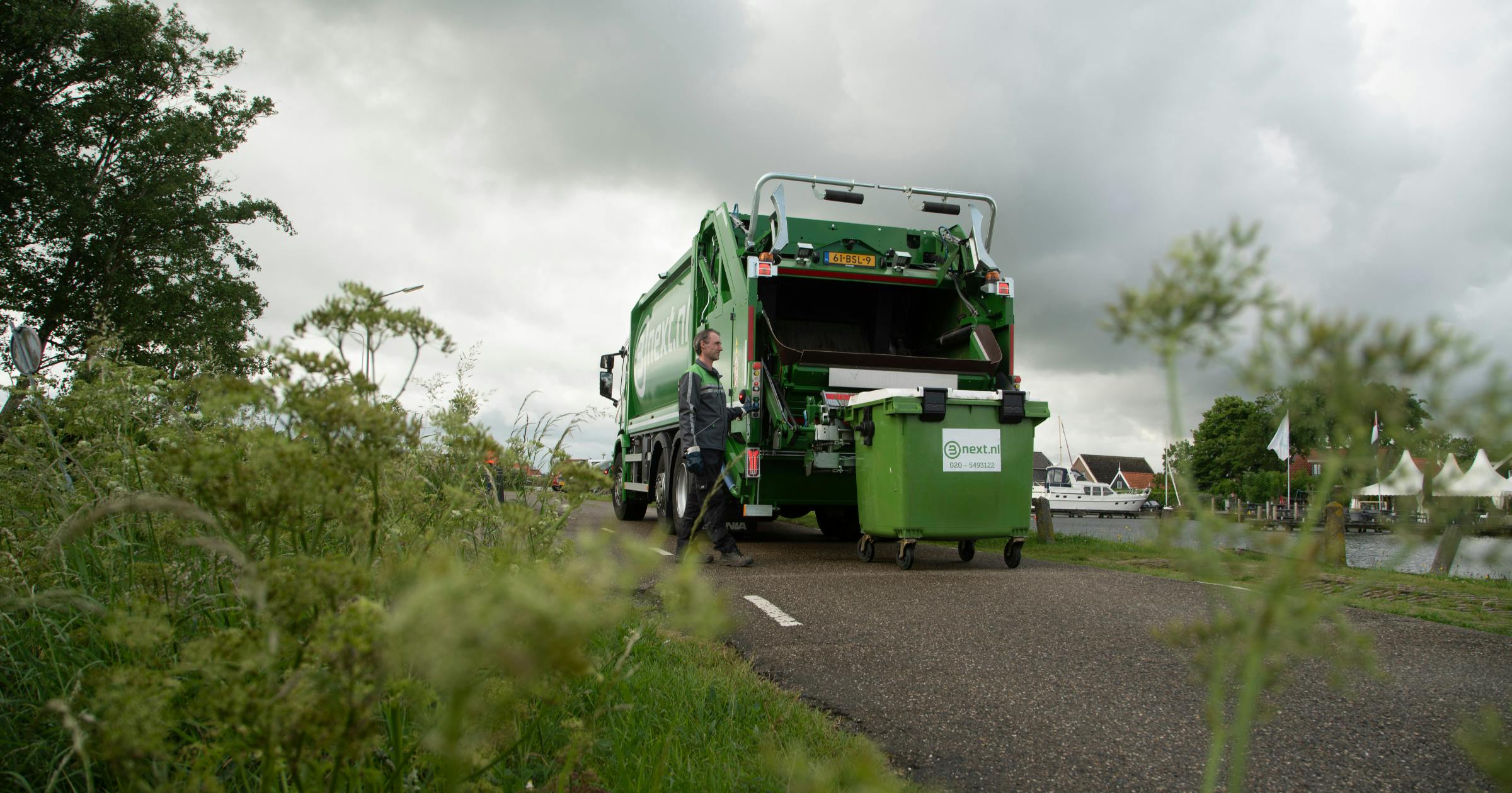 rolcontainer wordt opgehaald op een weg langs het water