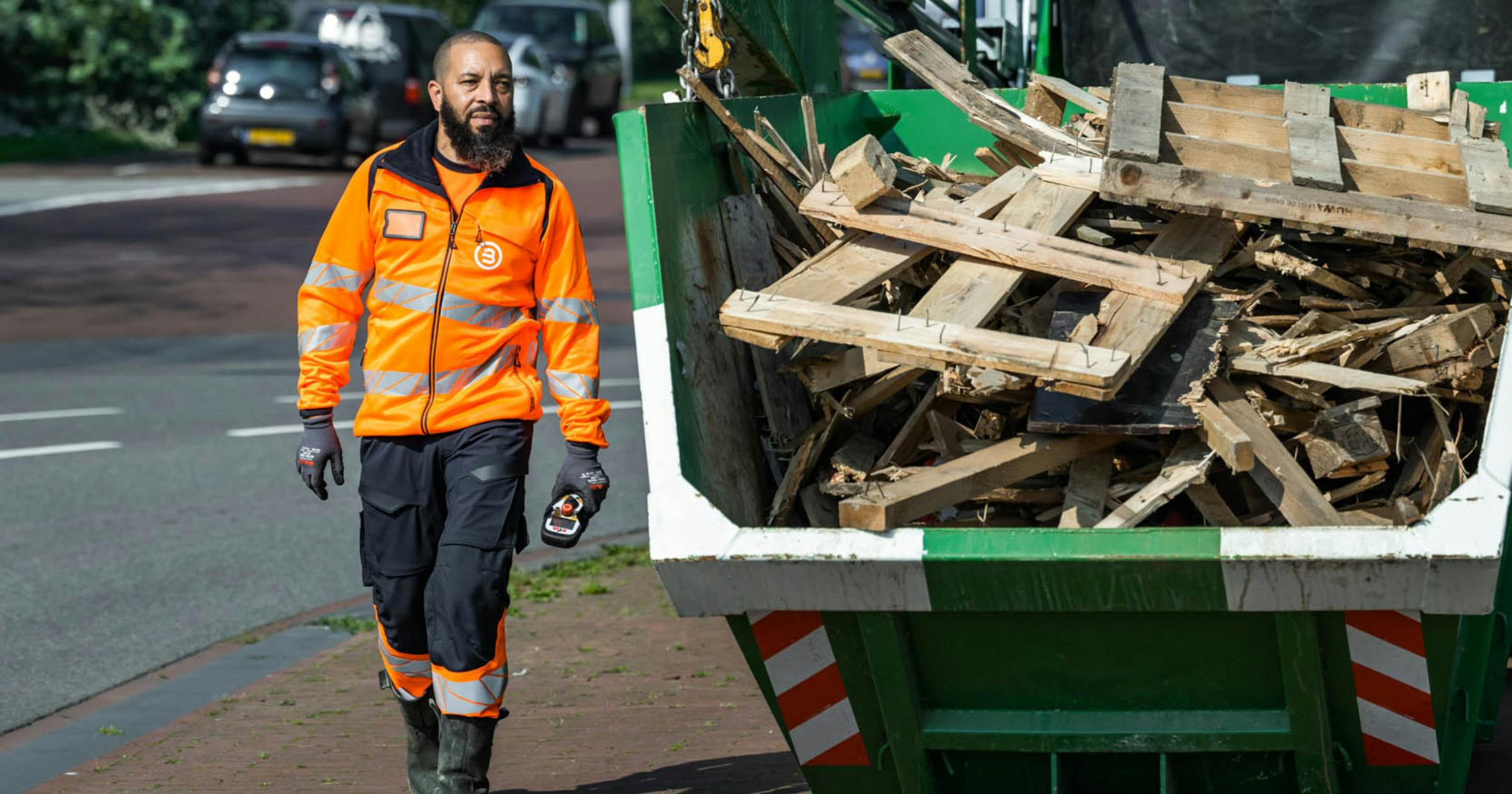 Man naast een container gevuld met afvalhout in een stedelijke omgeving