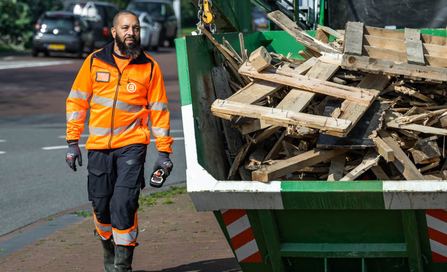 Man naast een container gevuld met afvalhout in een stedelijke omgeving