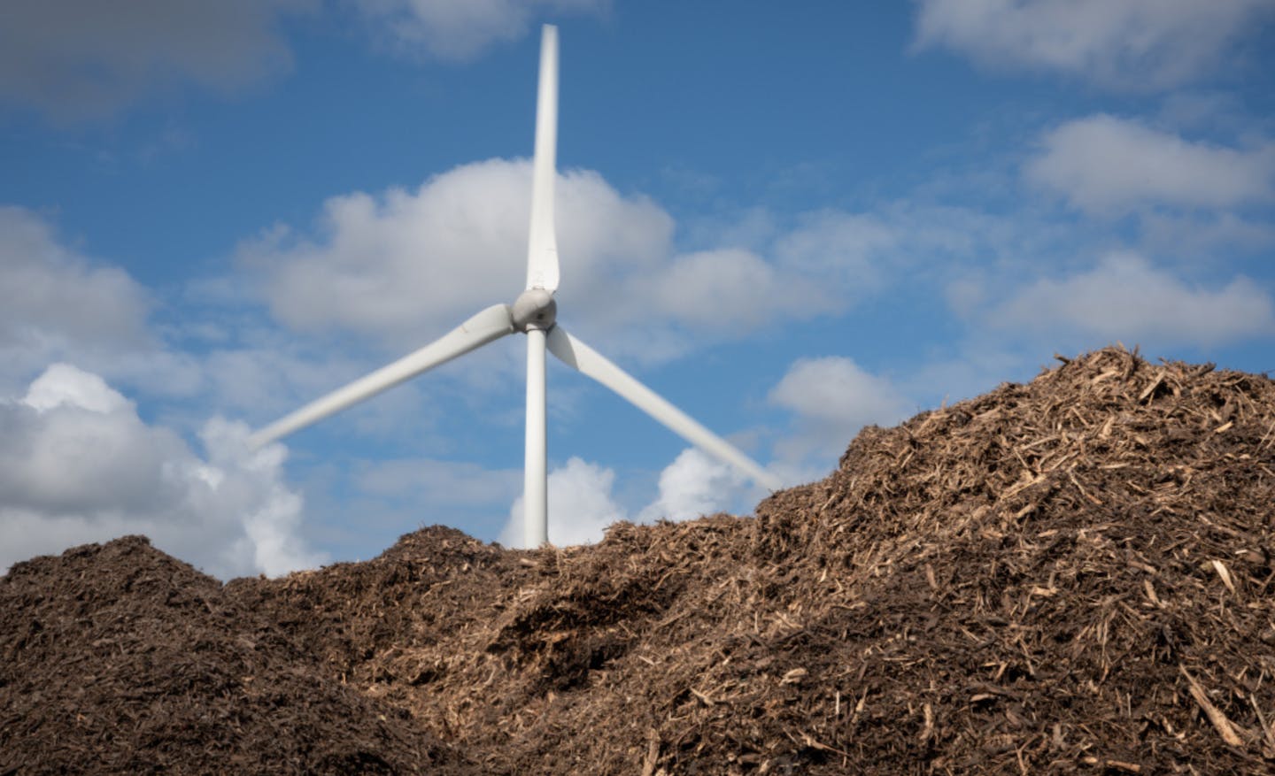 Een windmolen achter een berg compost tegen een blauwe lucht
