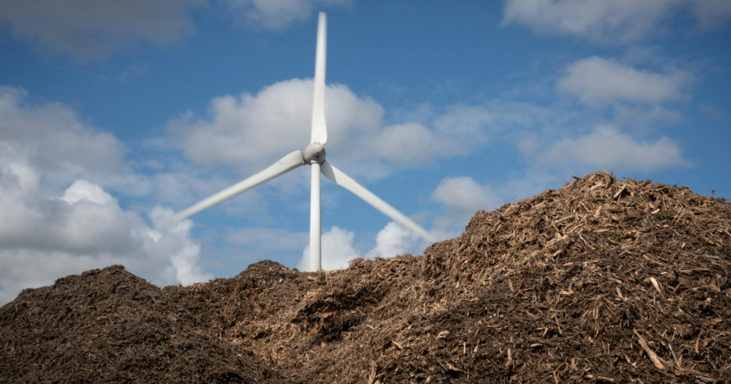Een windmolen achter een berg compost tegen een blauwe lucht
