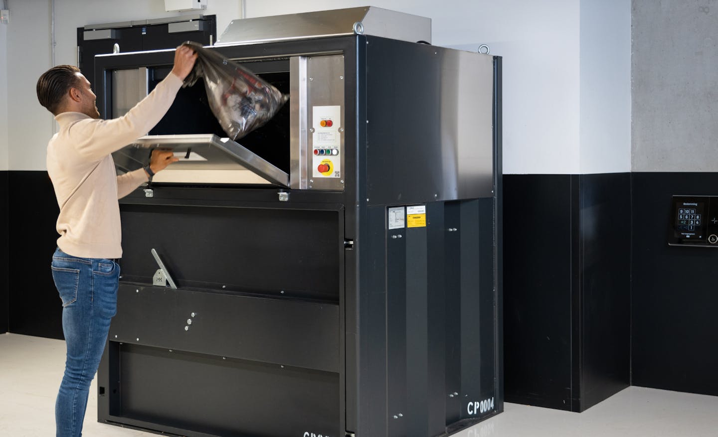 Man gooit afval in de perscontainer in de kelder van een kantoorgebouw