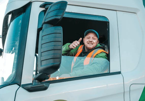 Blije man achter het stuur van een vrachtwagen met zijn duim omhoog