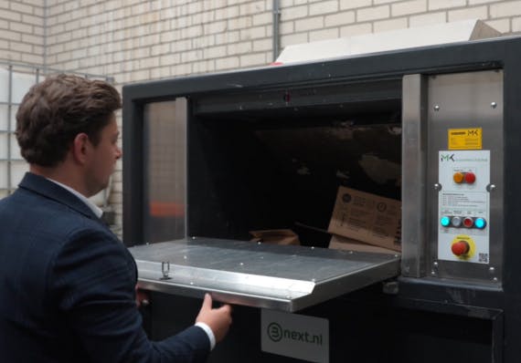 man gooit kartonnen dozen in een perscontainer