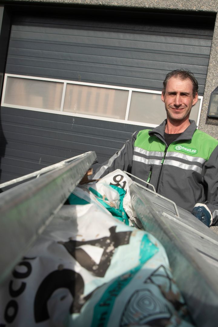 Bnext.nl chauffeur achter een container vol met restafval.