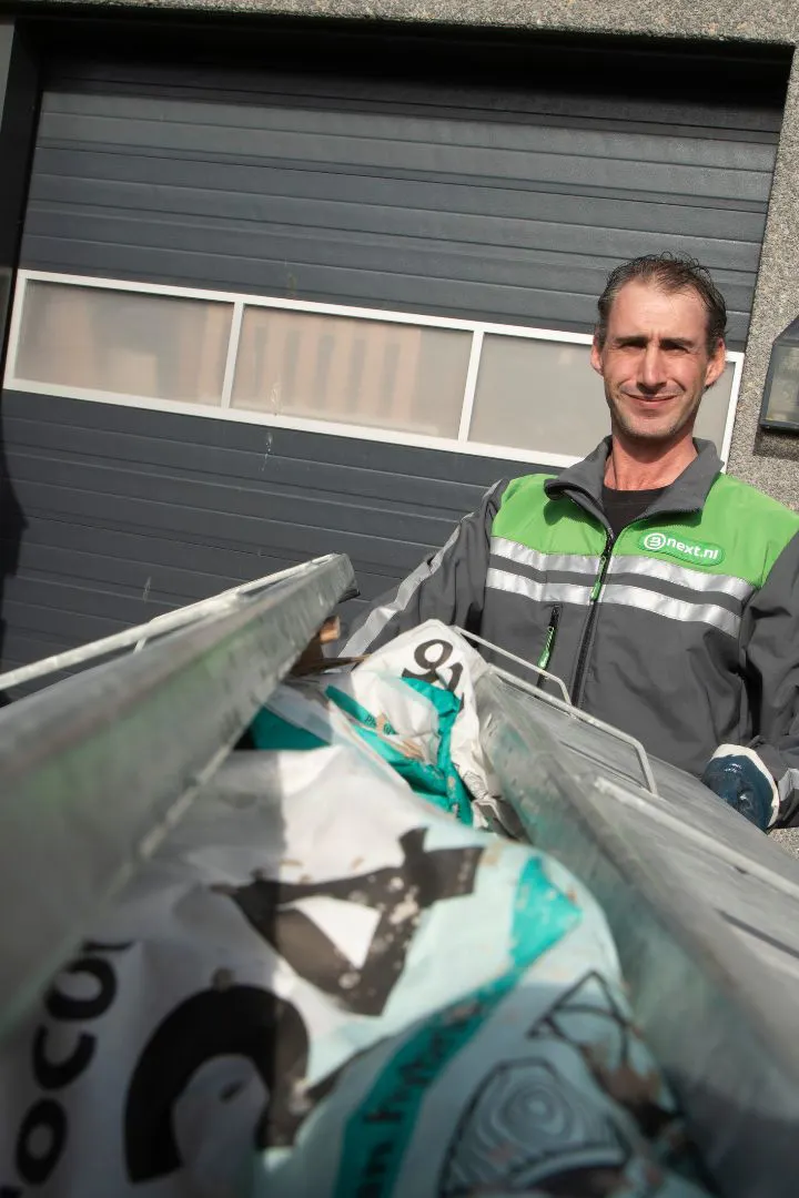Bnext.nl chauffeur achter een container vol met restafval.