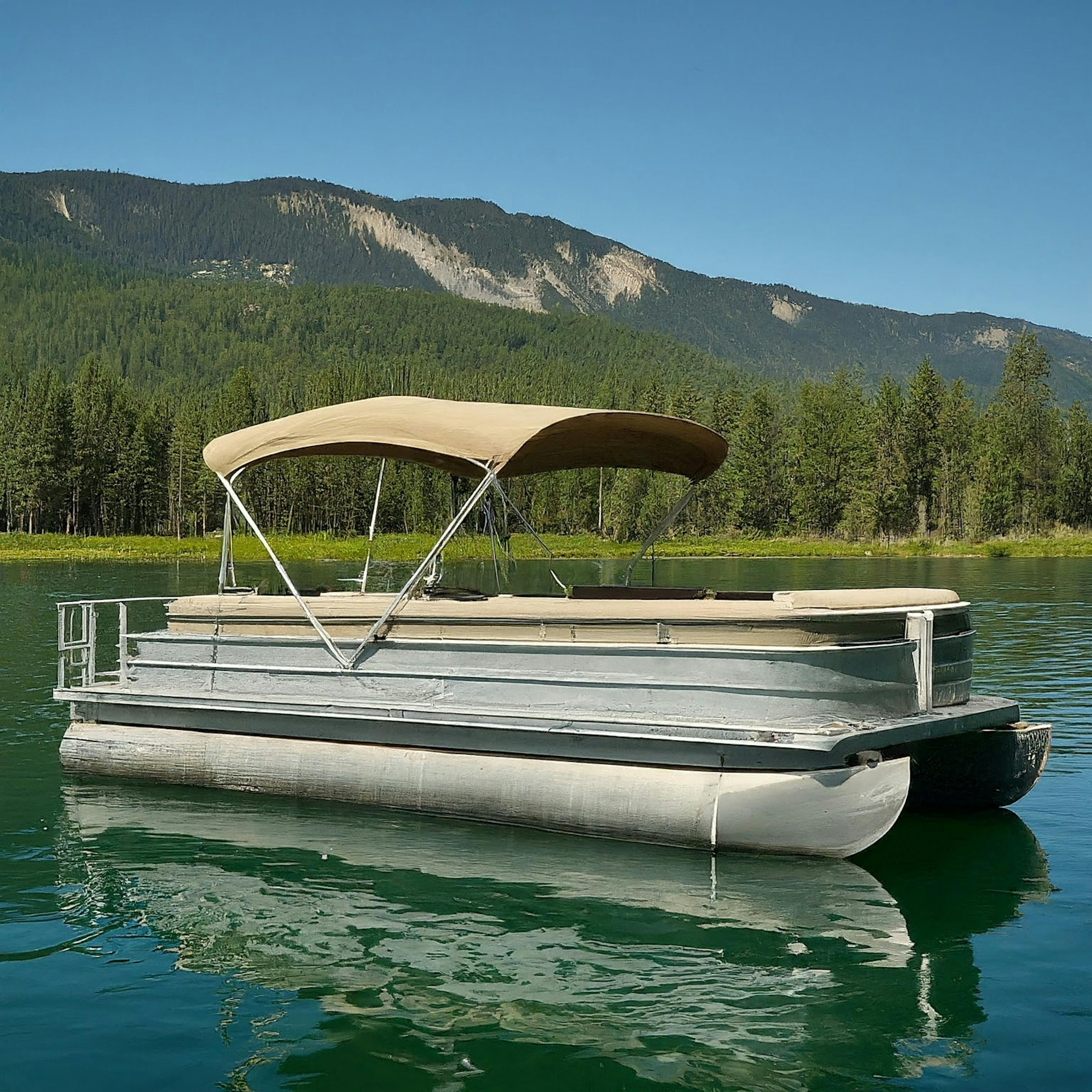 new Pontoon boat floating in the lake area with green forest and mountains on a background. Navigating the Waters of Pontoon Boat Pricing