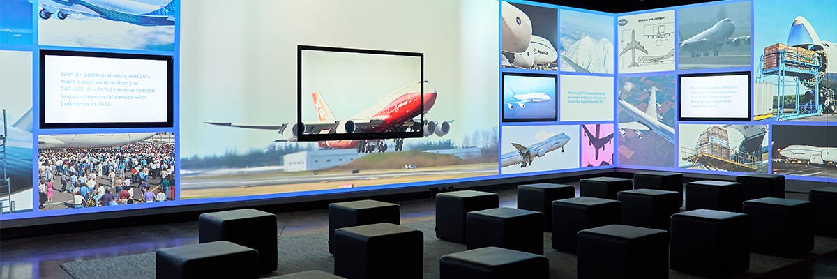 A liminal space with modular blocks of seating, surrounded by floor-to-ceiling projections of hundreds of Boeing 747 photos, historic films and footage from the sendoff flight.