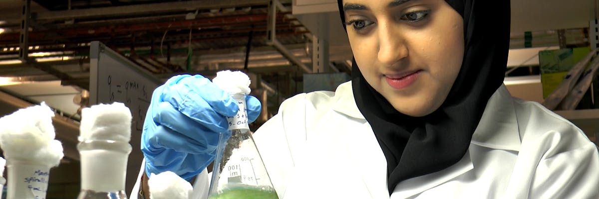 A scientist working with biofuels observes a flask as she swirls the fluid within