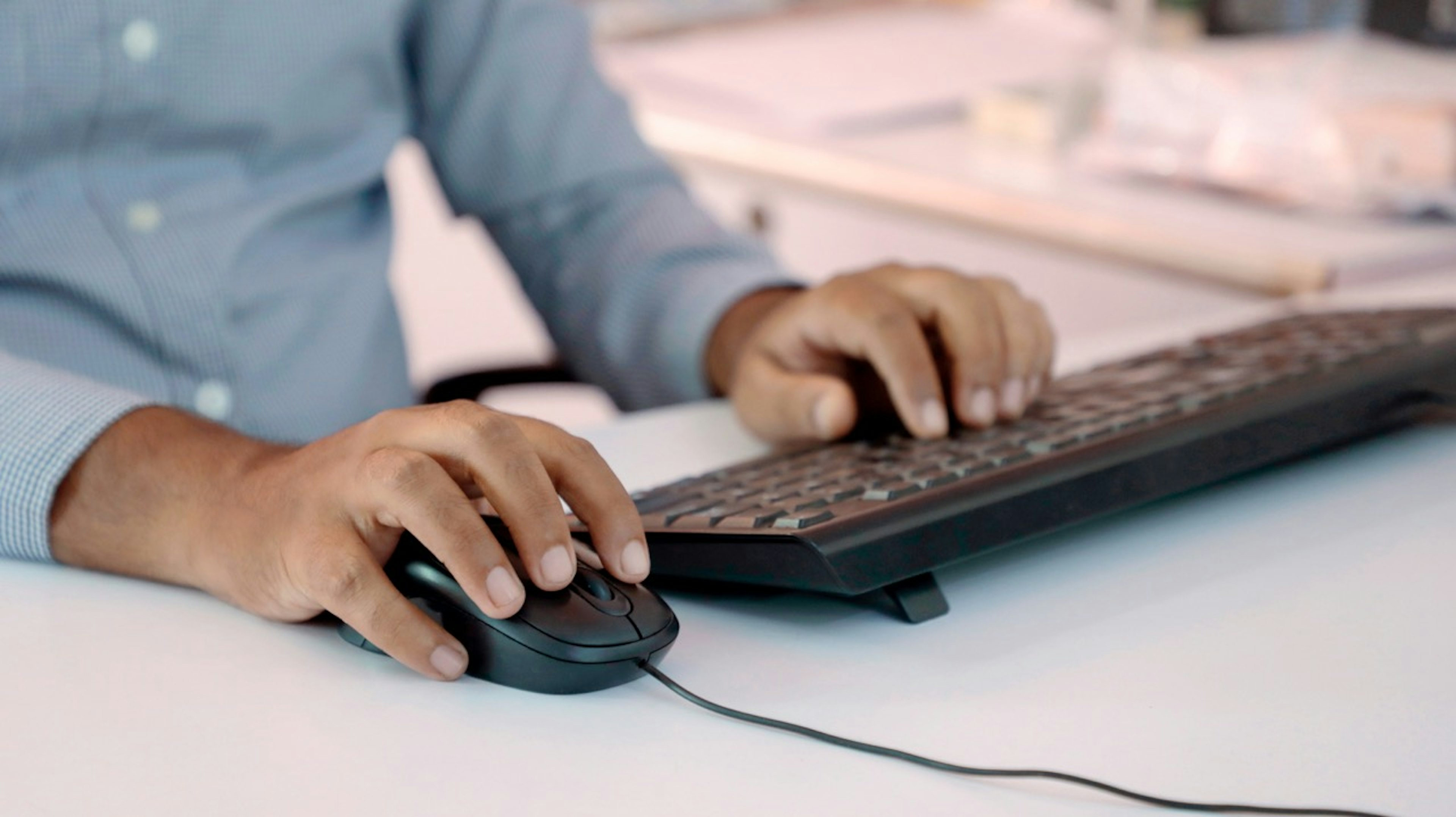 Hands using a computer mouse and keyboard at a desk, representing online or self-service work.