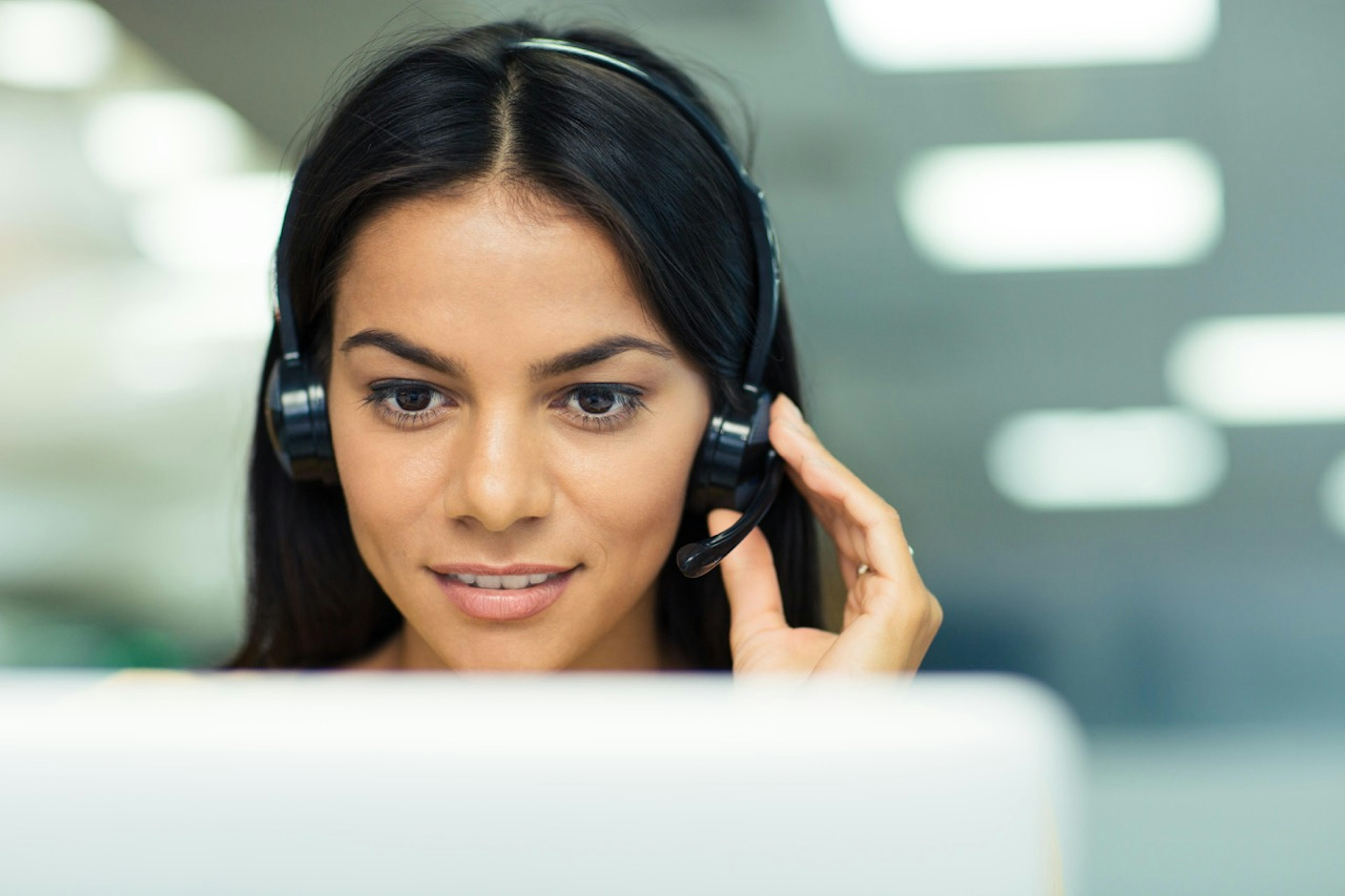 Customer support agent wearing a headset focuses on a computer screen while assisting a customer.
