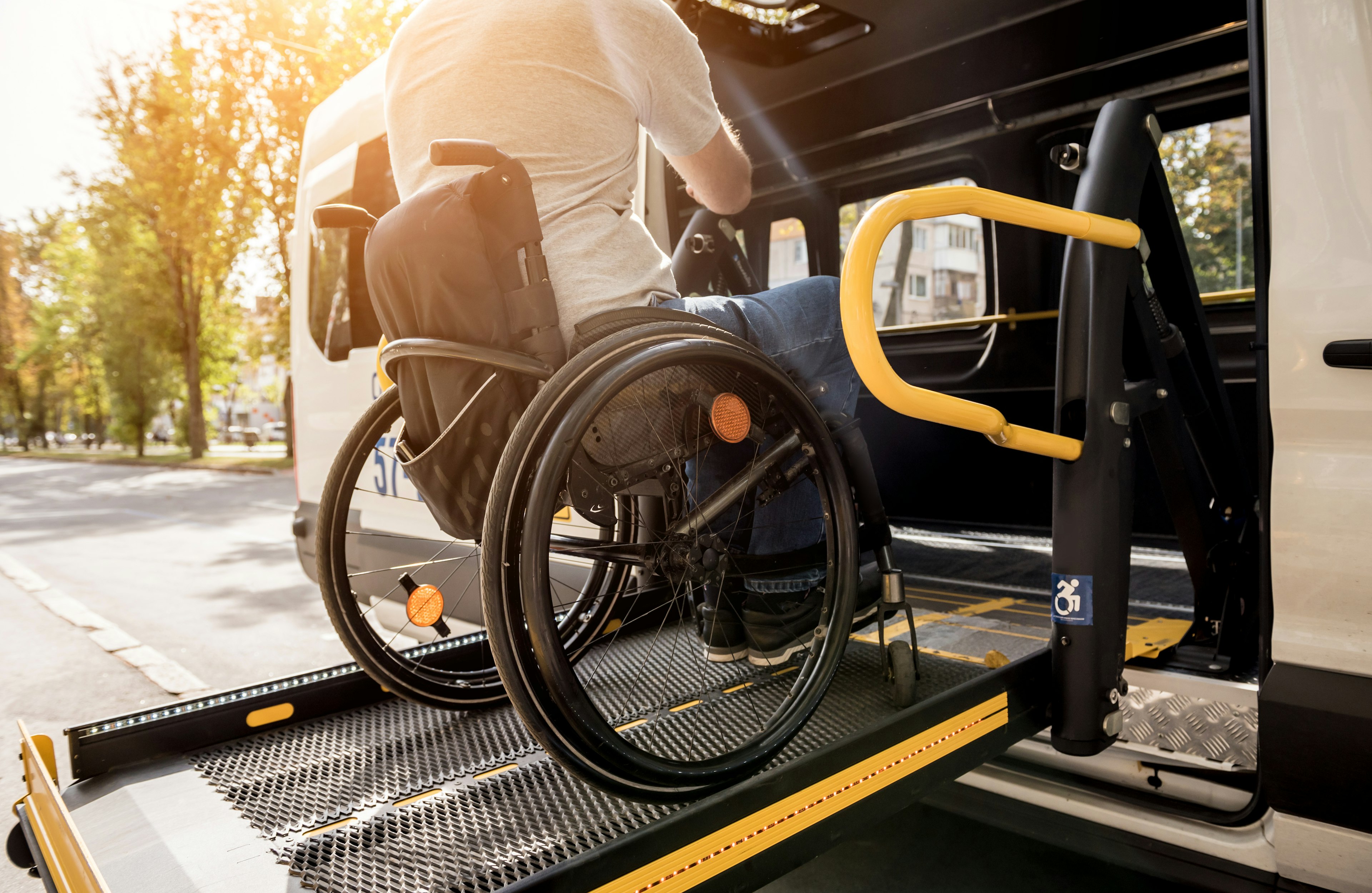 Wheelchair user boarding an accessible transit van via a deployed ramp, with safety rails visible in daylight.