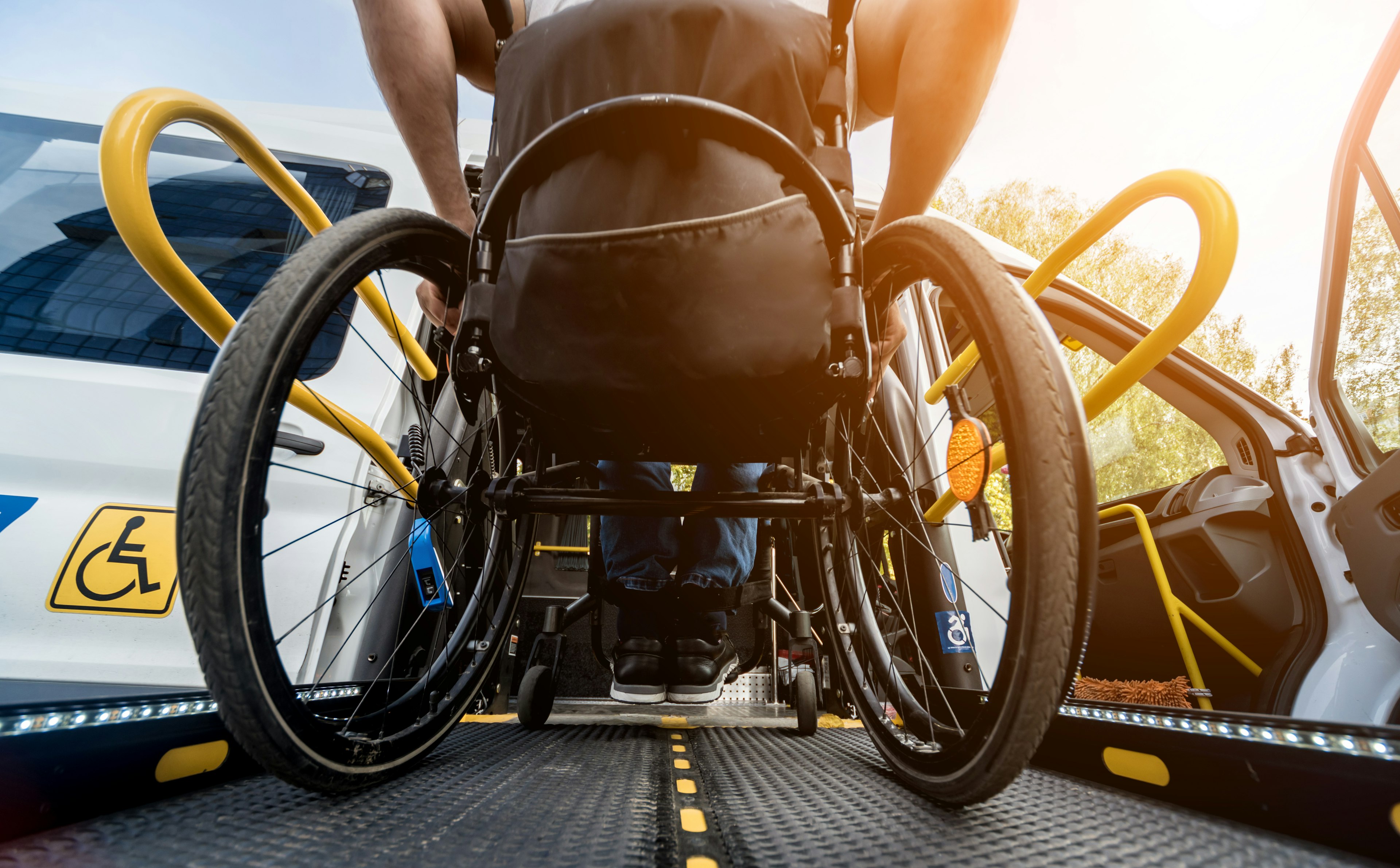 Wheelchair user boarding an accessible transit van via a deployed ramp, with safety rails visible in daylight.