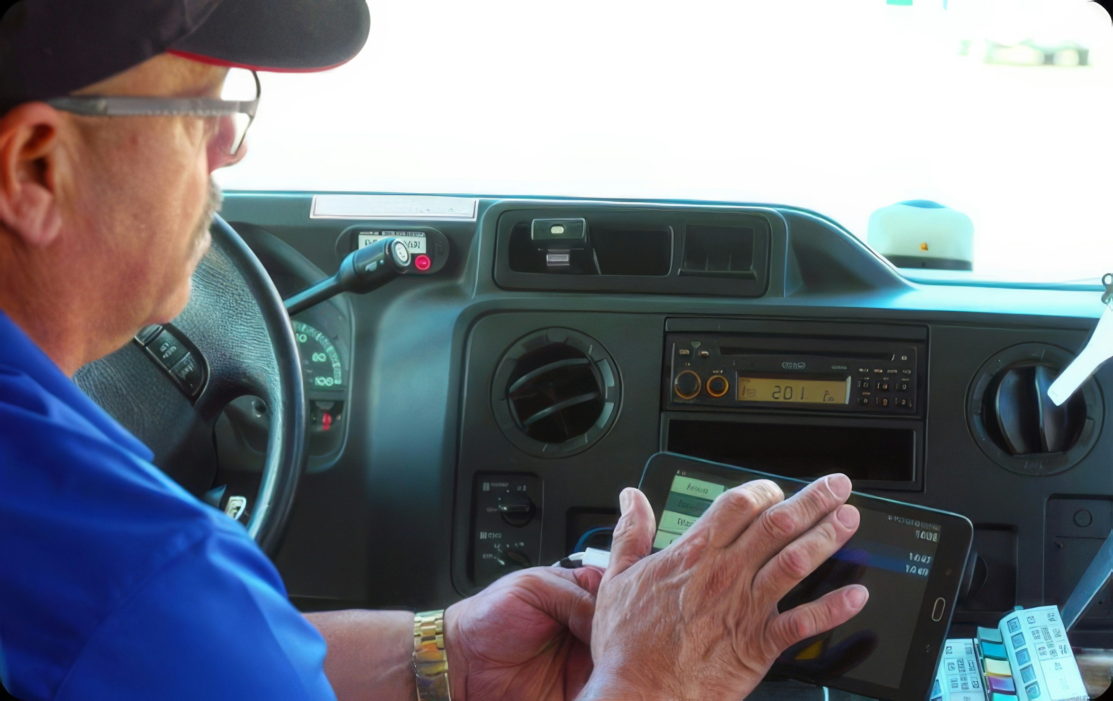 Transit driver seated in the cab uses a handheld tablet to review or enter trip information while the vehicle is parked.