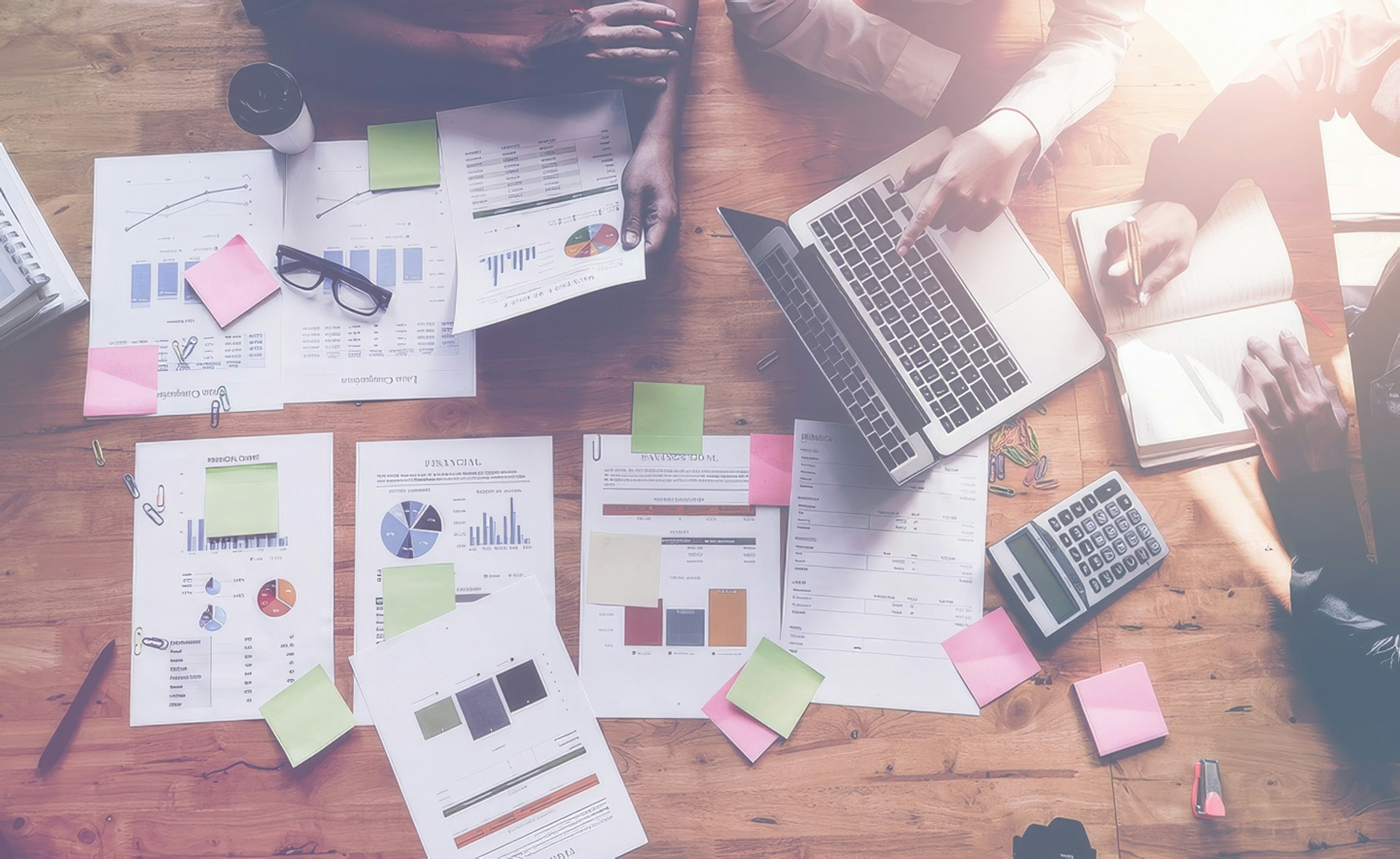 Overhead view of a team collaborating around a table with charts, reports, sticky notes, and laptops.