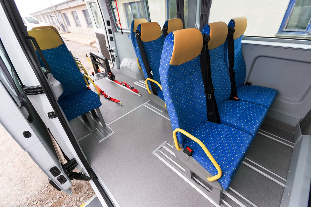 Interior of a bus showing overhead handholds and a ceiling-mounted security camera above standing passengers.