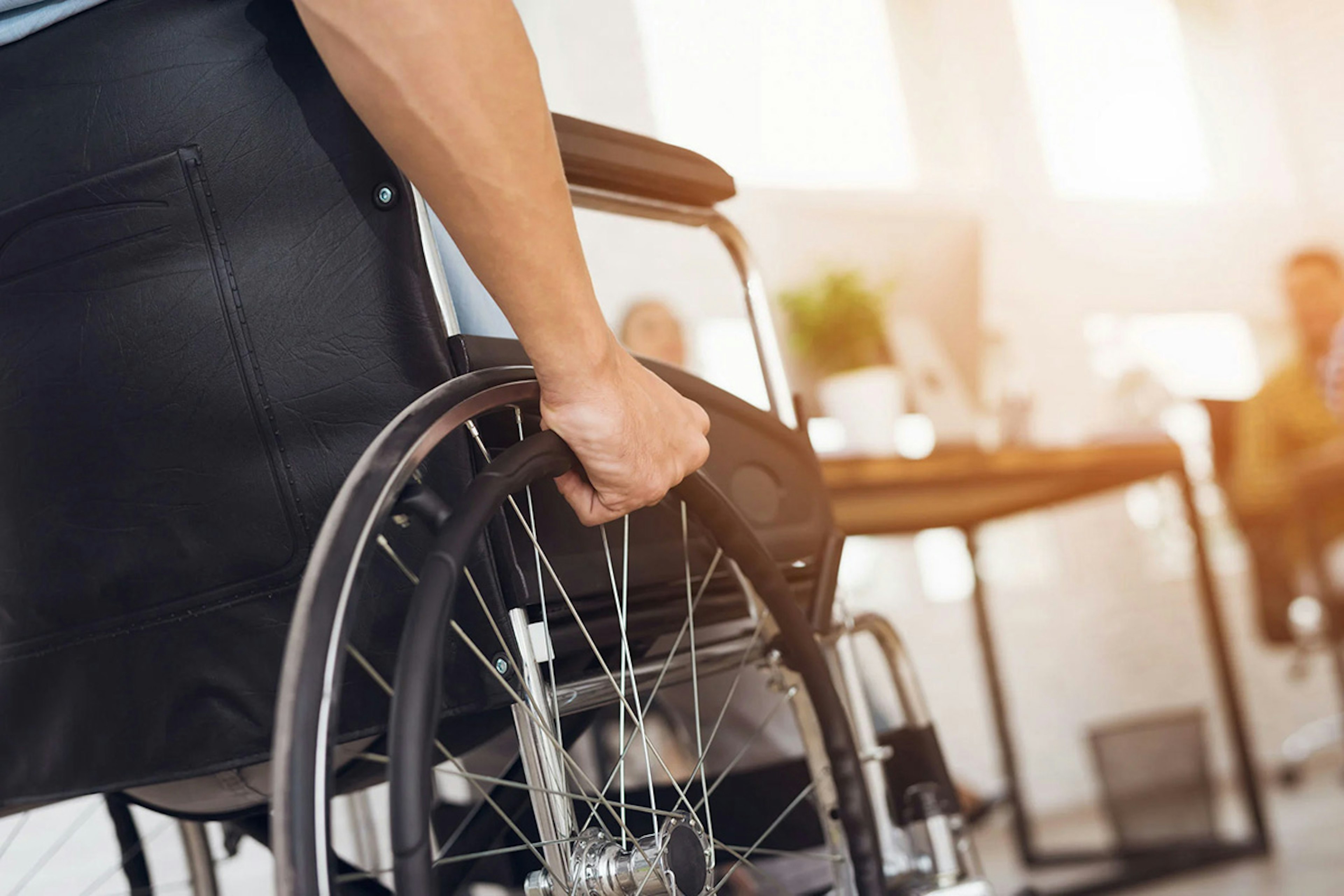 Close-up of hands gripping a wheelchair wheel inside a public building.