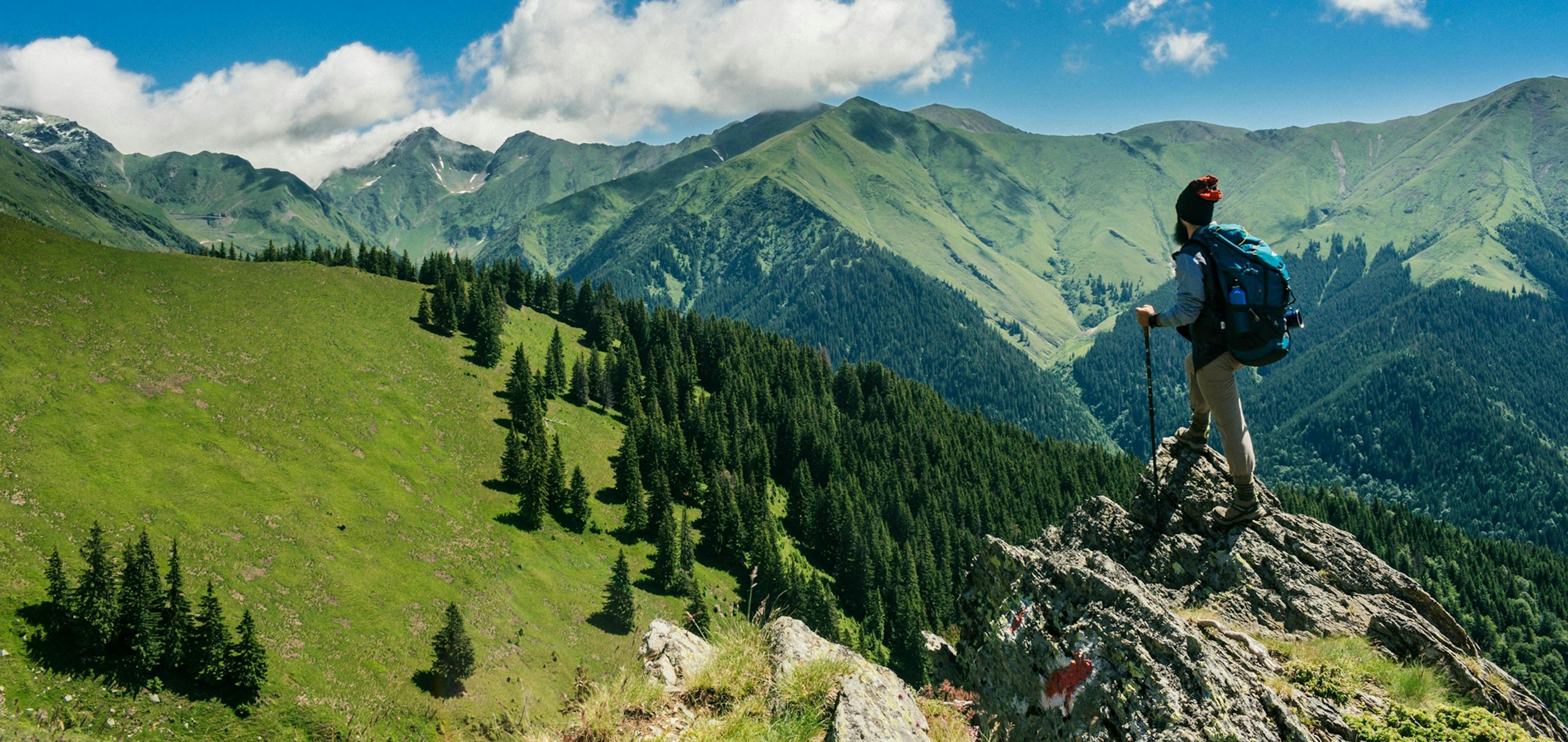 letní panoramata hor, Alpy, na vrcholku stojí turista s batohem a hůlkami