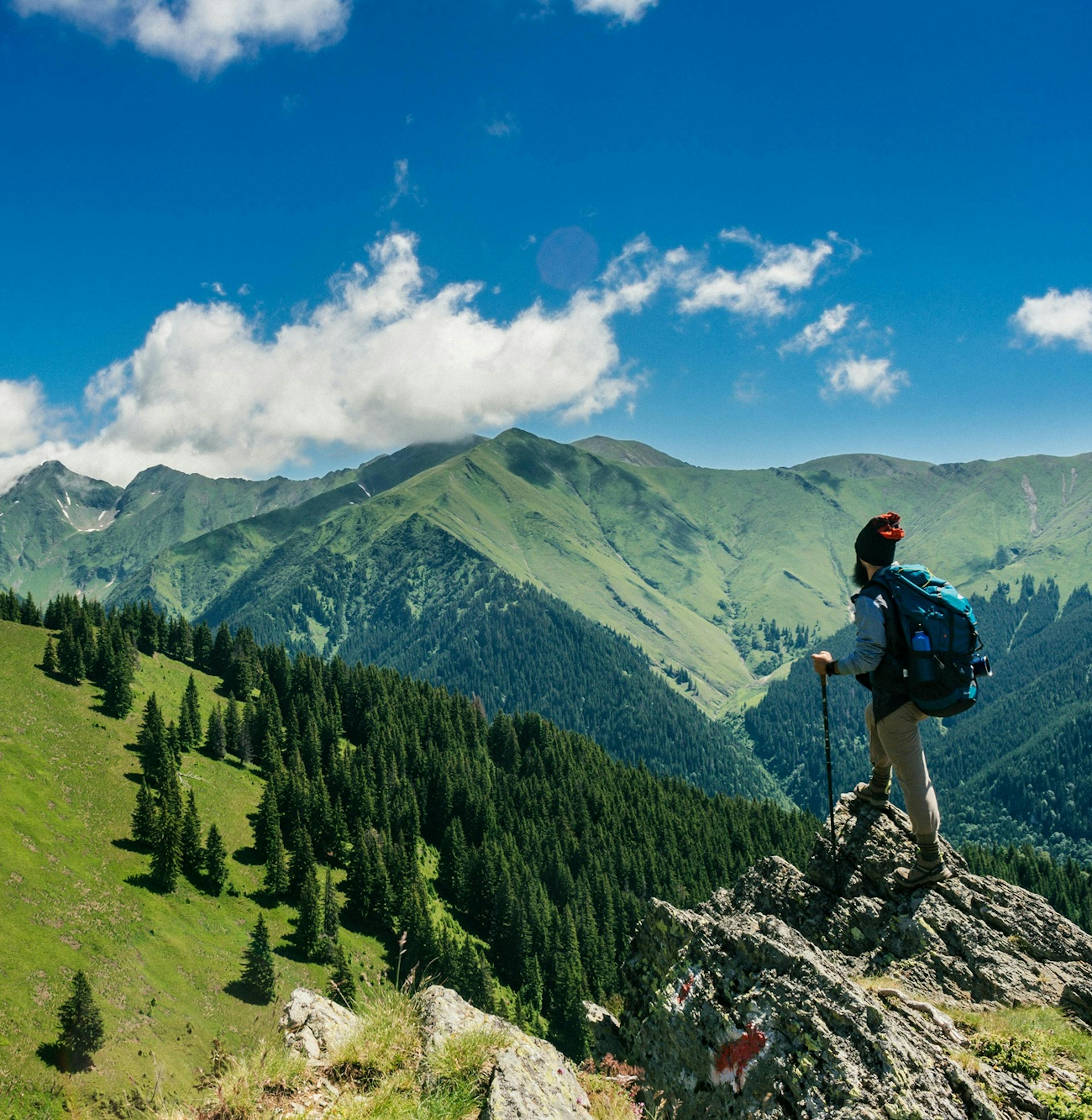 letní panoramata hor, Alpy, na vrcholku stojí turista s batohem a hůlkami