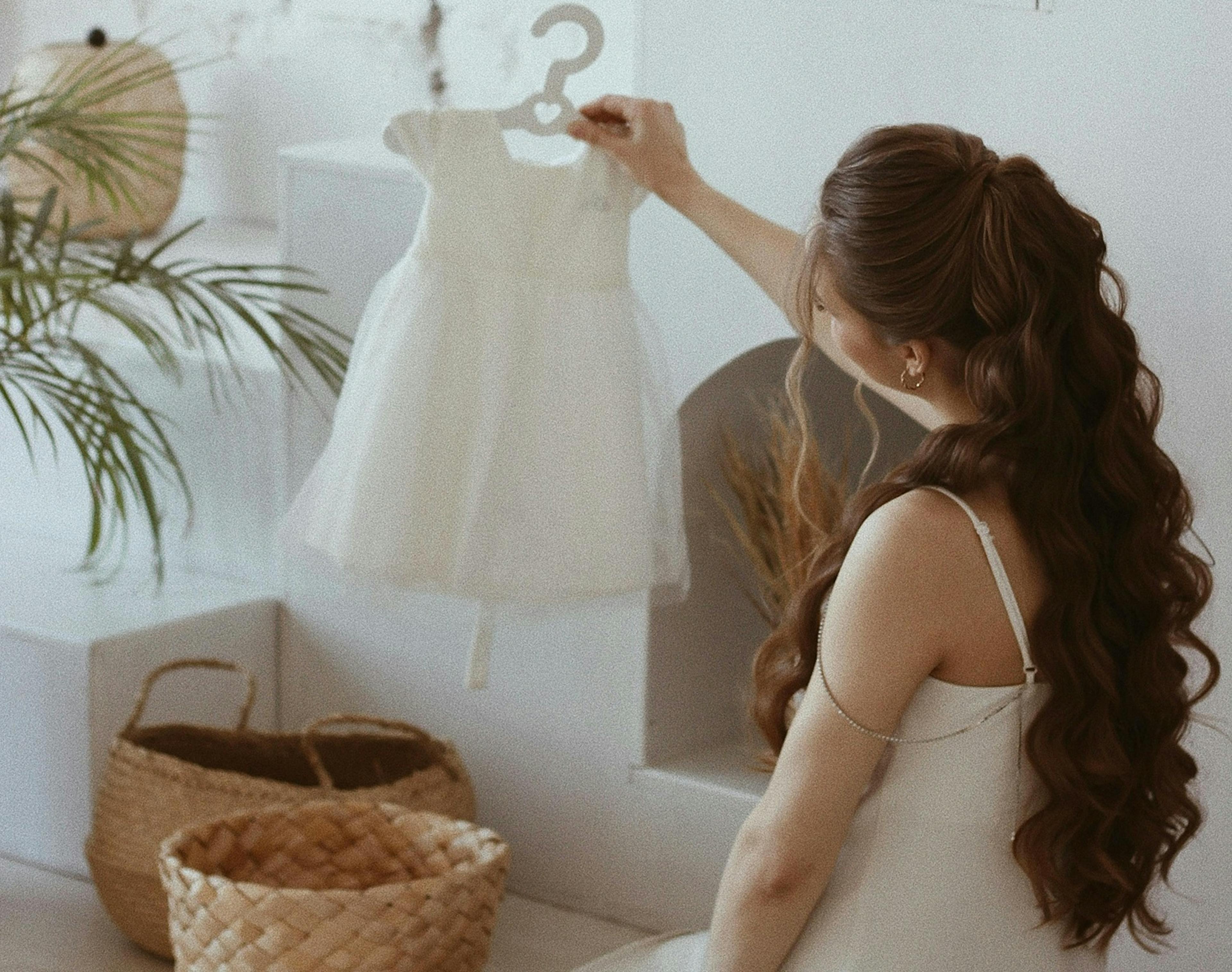 žena si prohlíží dětské bílé šatičky na ramínku