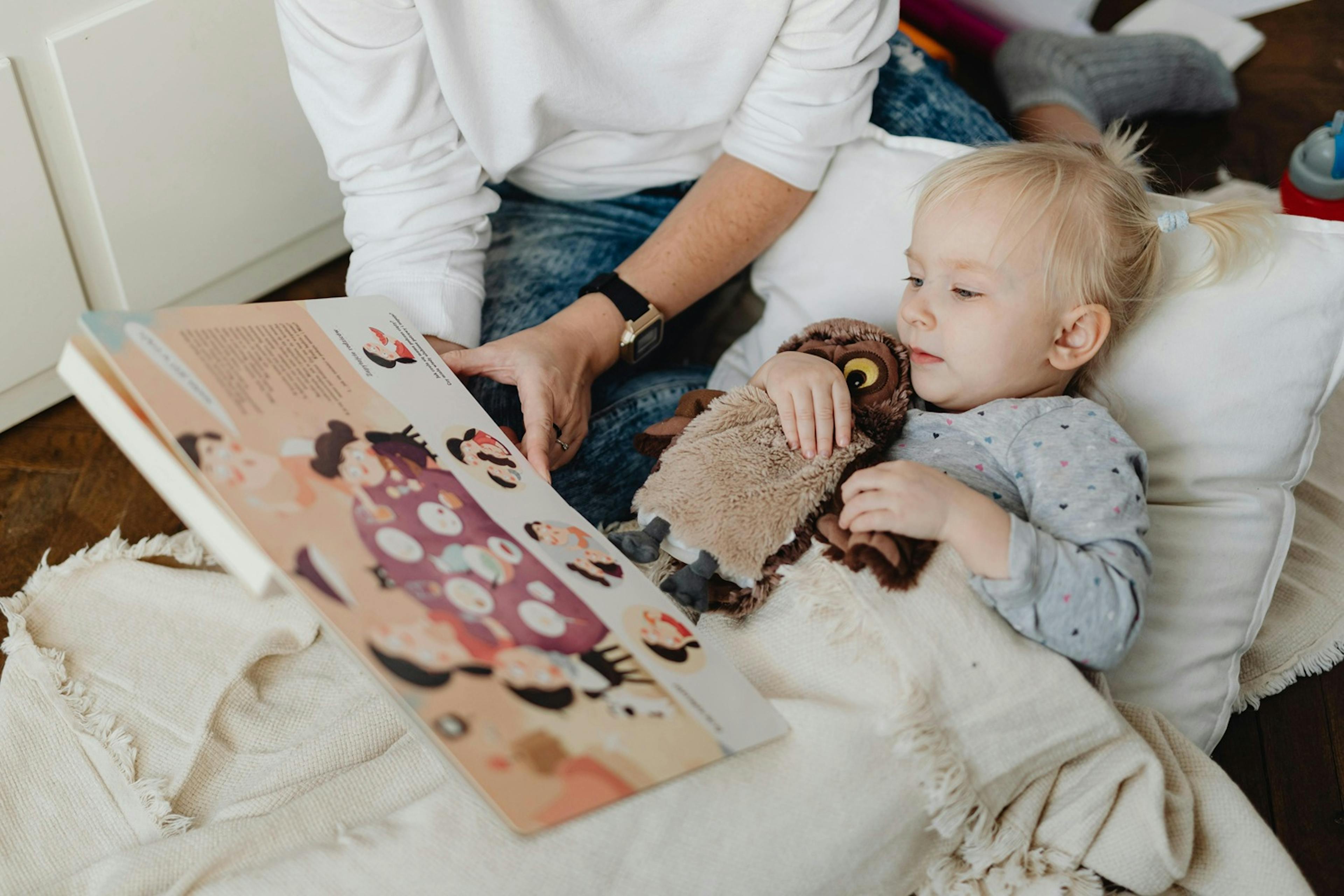 malá holčička leží v postýlce a s maminkou si prohlíží obrázkovou knížku