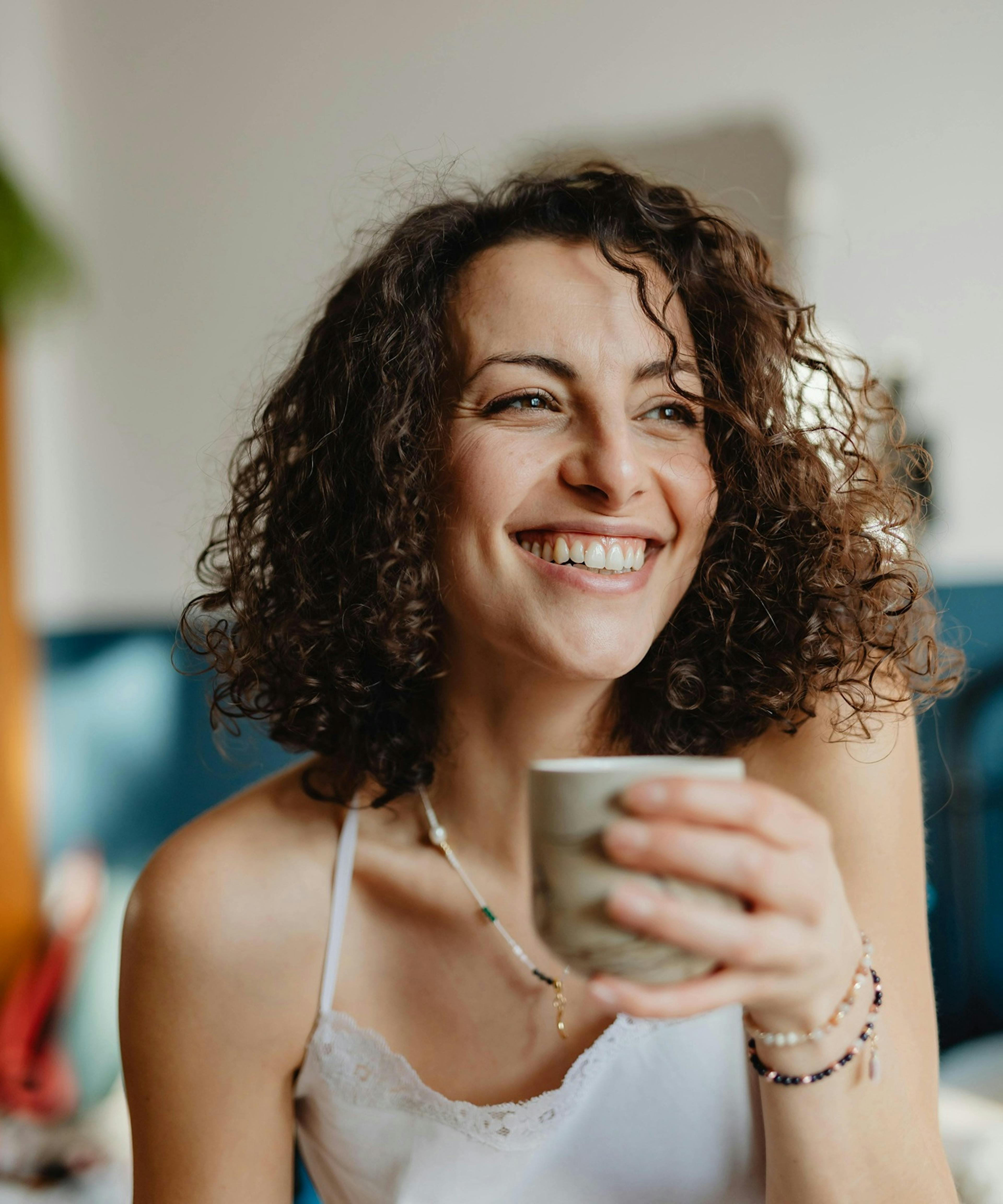 mladá žena v detailu, drží v ruce hrníček a usmívá se