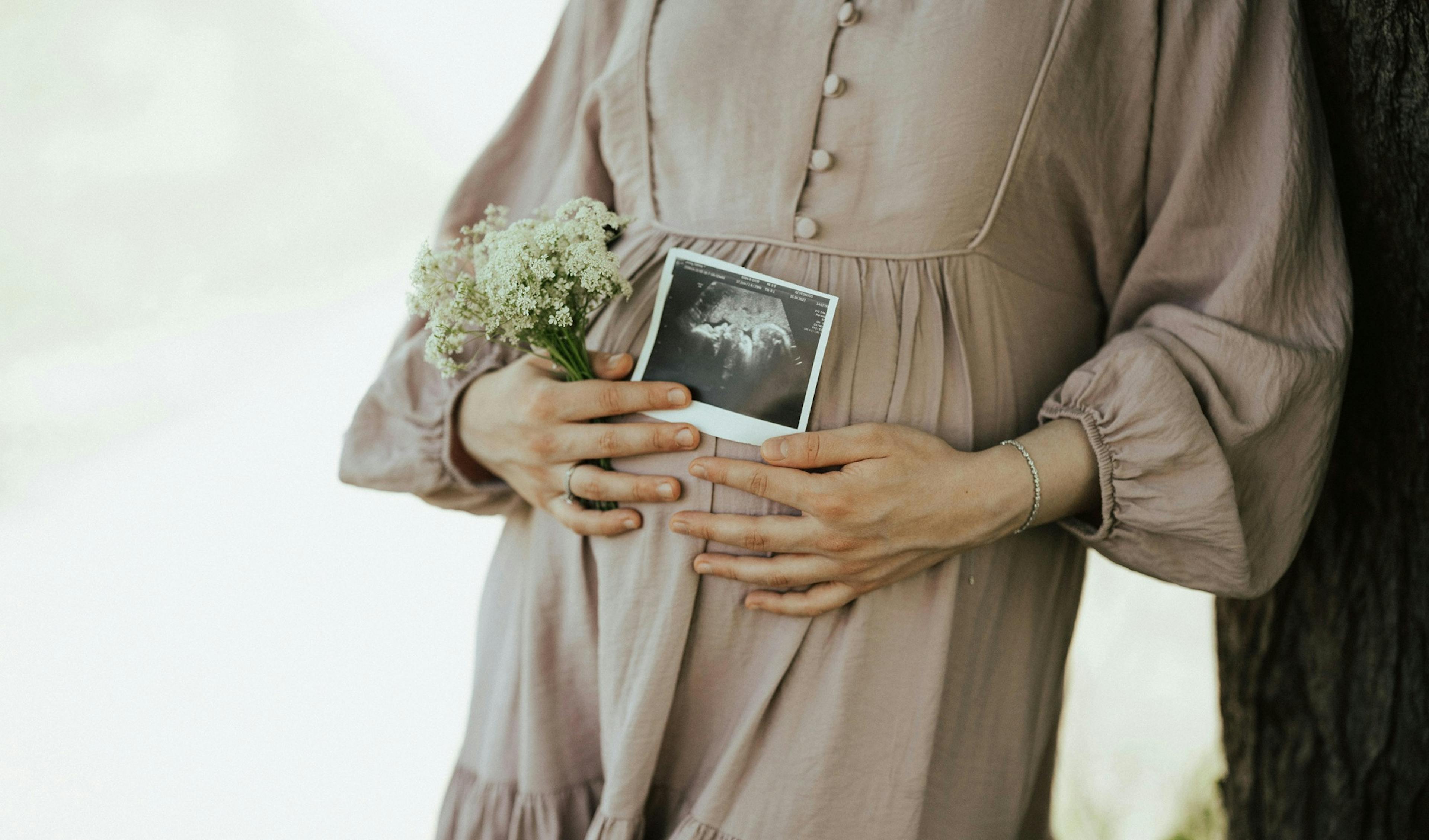 těhotná žena, detail na bříško, v ruce drží kytičku snímek miminka
