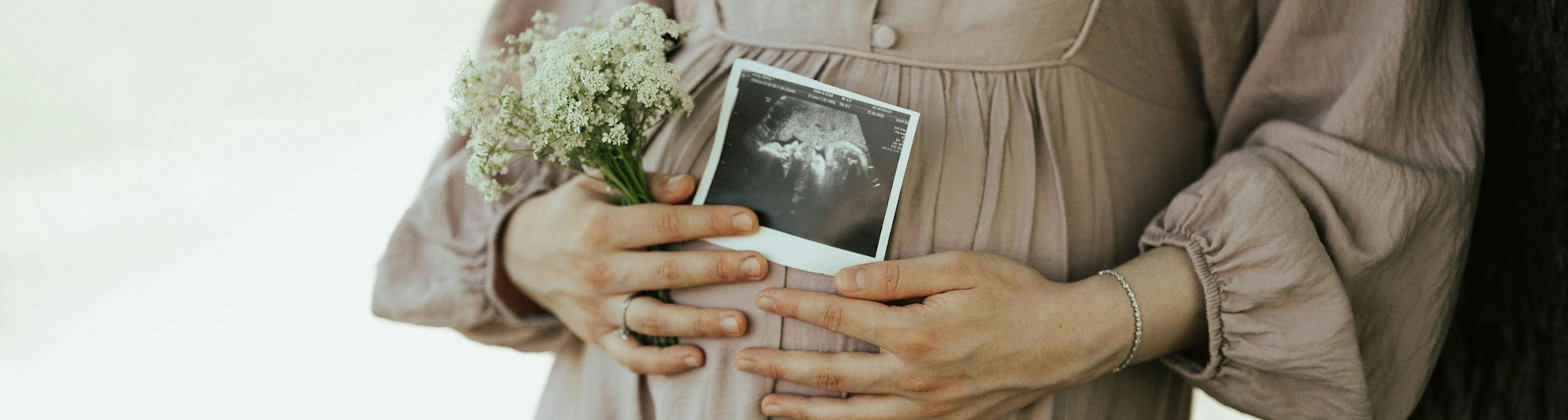 těhotná žena, detail na bříško, v ruce drží kytičku snímek miminka