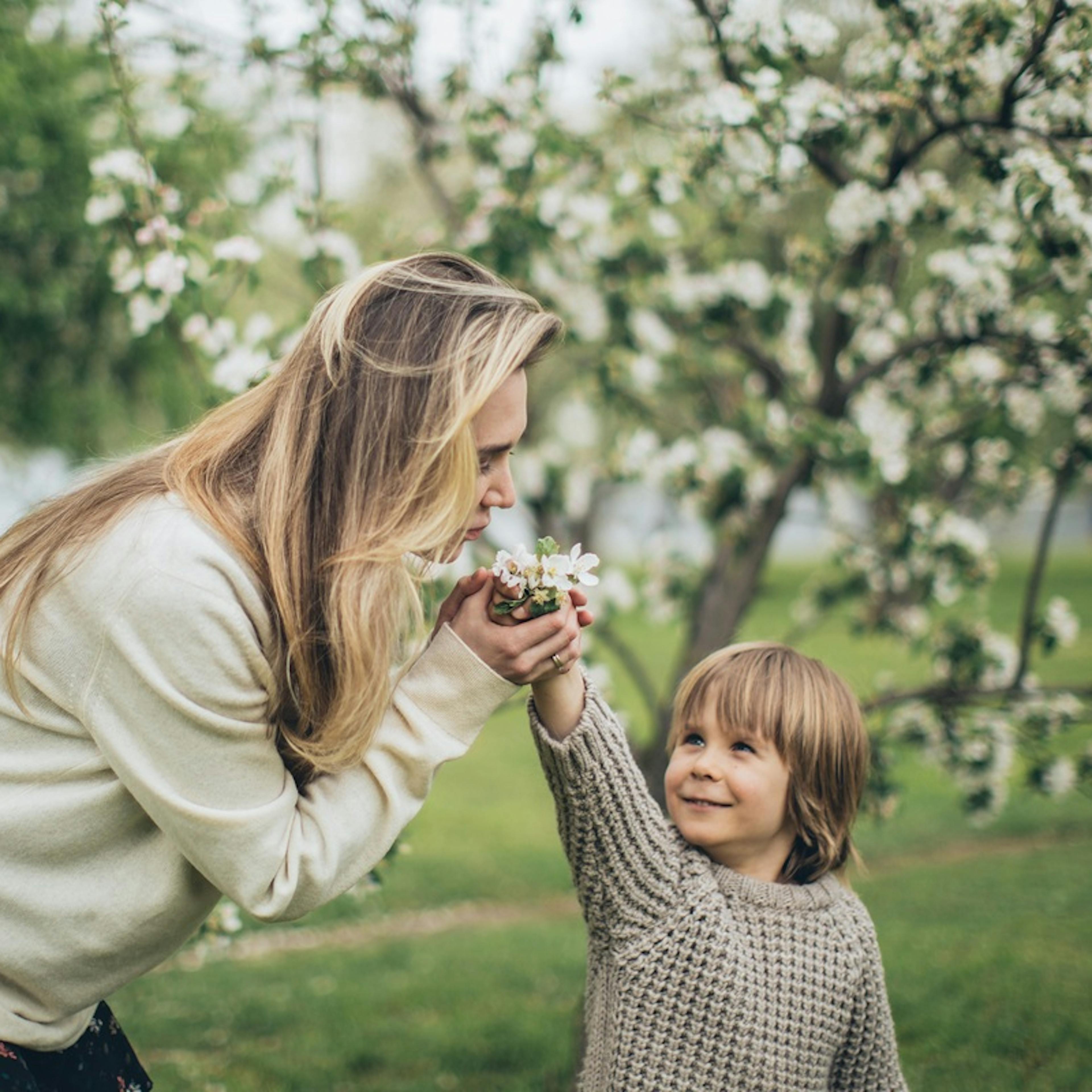 Maminka se synem v rozkvetlé zahradě, čichají ke květům rozkvetlého stromu