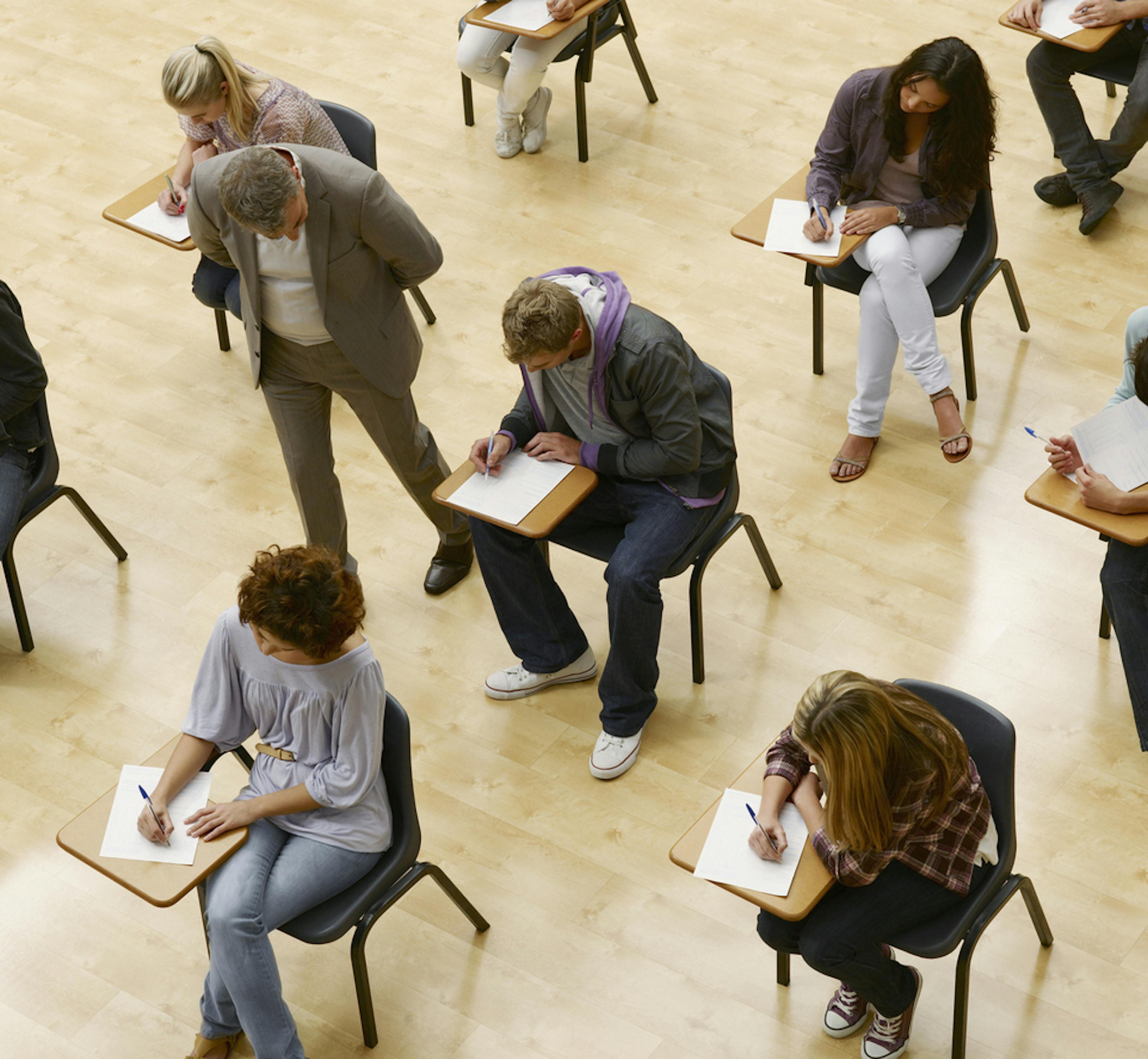 Studenti durante esame di maturità con prof che controlla tra i banchi