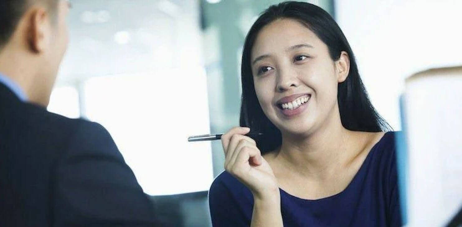 women smiling and holding up a pen while talking to man