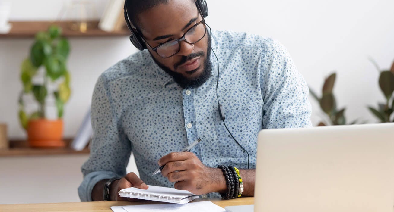 Man writing notes while having an online meeting.