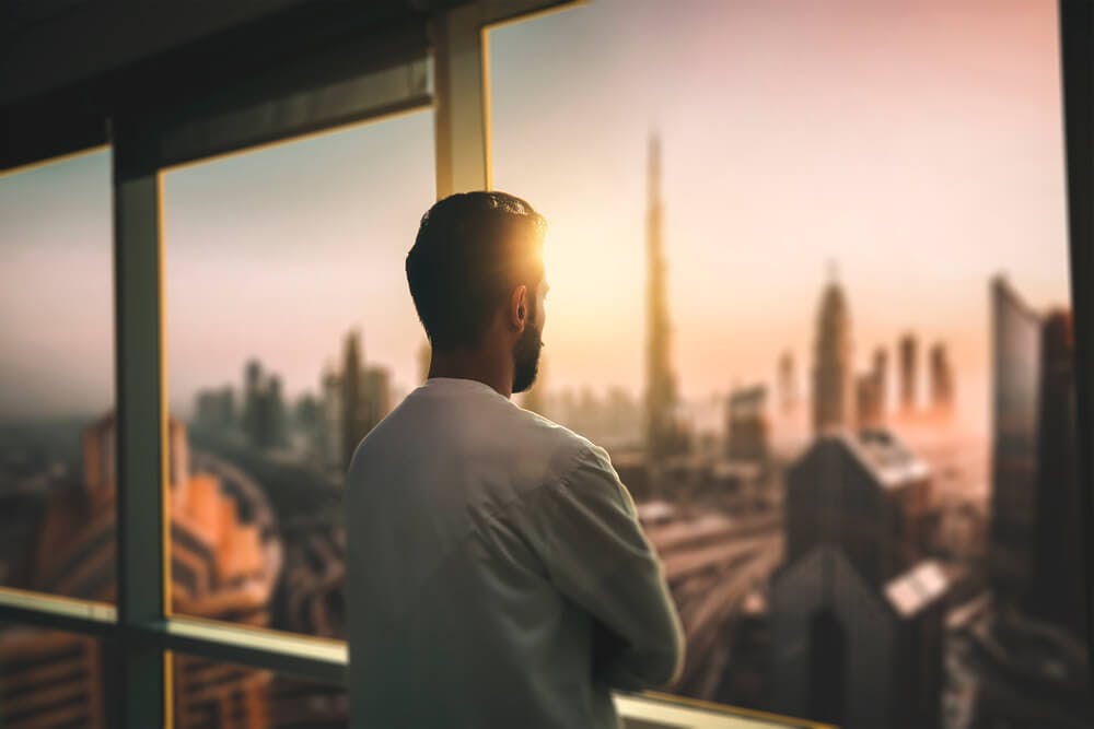 young man looking out office window during sunset