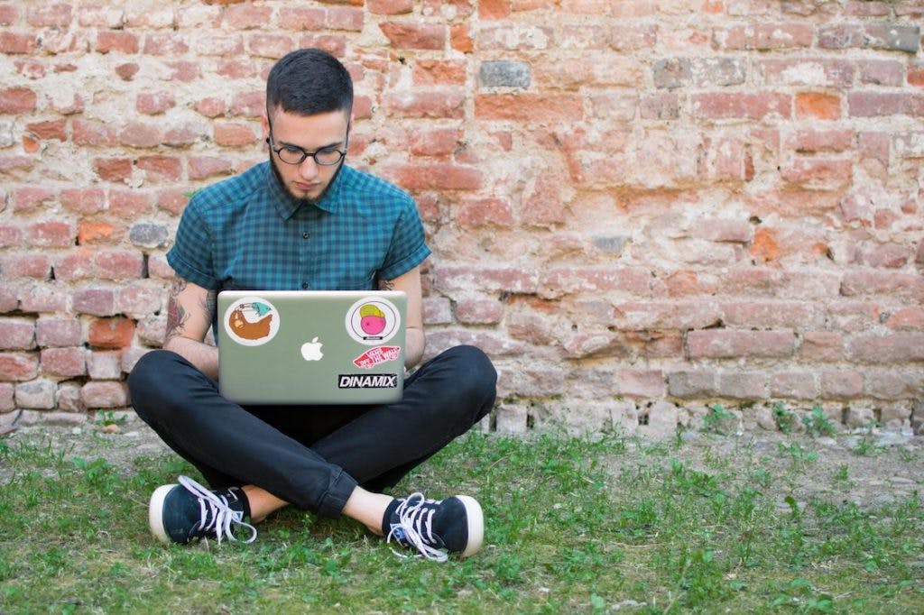 a man with glasses cross-sitting and using his laptop